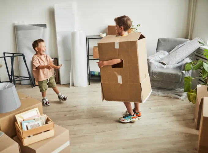 Two young boys laughing and playing with moving boxes.
