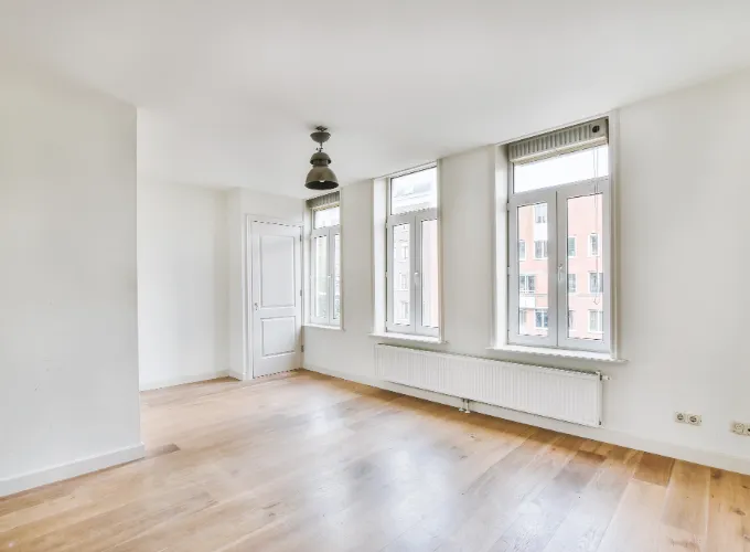 Interior of empty apartment with windows, wood floors, and white walls.